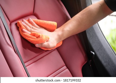 Man's Hand Cleaning Red Interior In Luxury Car With Microfiber Cloth. Hand Wipe Down Leather Seat Of Sports Car.  Interior Car Detail And Leather Seat Repair & Cleaning Background. Car Wash Concept.