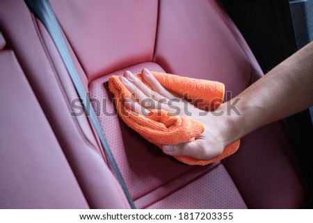 Man's hand cleaning red interior in luxury car with microfiber cloth. Hand wipe down leather seat of sports car.  Interior car detail and leather seat repair & cleaning background. Car wash concept.
