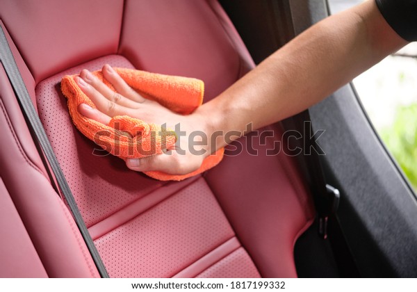 Man's hand cleaning red interior in luxury car
with microfiber cloth. Hand wipe down leather seat of sports car. 
Interior car detail and leather seat repair & cleaning
background. Car wash
concept.
