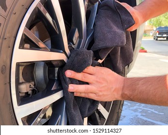 Man's hand cleaning wheel and tire with black microfiber cloth. Hand wipe down shiny rims surface of car. Car detailing and car wash concept , San Diego, USA, October, 11th, 2019 - Powered by Shutterstock