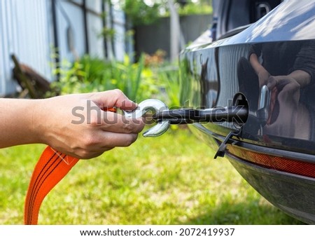 A man's hand clings a tow rope to a tow hook in a passenger car, close-up. Summer