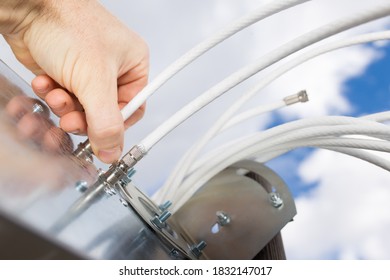 Man's hand connecting Cable to 4G antenna close up with sky on background.