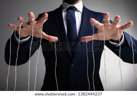 Man's Hand Controls The Puppet With The Fingers Attached To Threads Against Gray Background