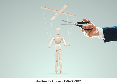 A man's hand cuts the threads between the puppeteer and the puppet with scissors. The concept of liberation from slavery, freedom, shadow government, world conspiracy, manipulation, control