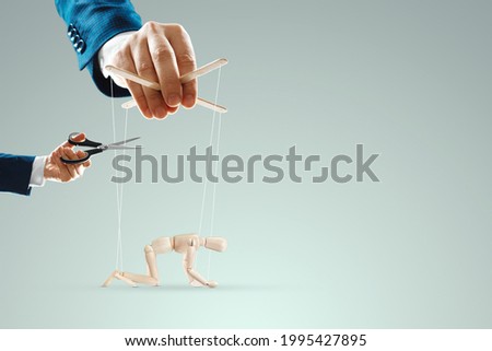 A man's hand cuts the threads between the puppeteer and the puppet with scissors. The concept of liberation from slavery, freedom, shadow government, world conspiracy, manipulation, control