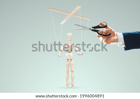 A man's hand cuts the threads between the puppeteer and the puppet with scissors. The concept of liberation from slavery, freedom, shadow government, world conspiracy, manipulation, control