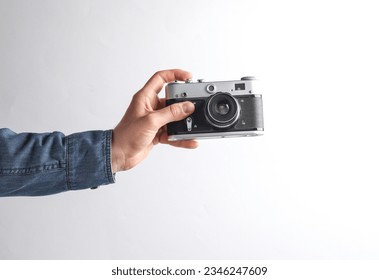 Man's hand in denim shirt holding retro film camera on gray background - Powered by Shutterstock