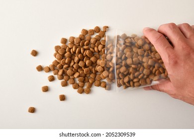 Man's Hand Dropping Dog Kibble From A Clear Plastic Bag Onto A White Table. Top View. Horizontal Composition.