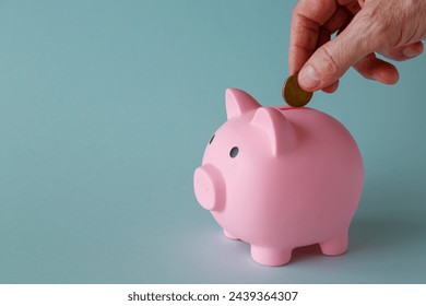 A man's hand drops a coin into a piggy bank. The concept of savings and investments. - Powered by Shutterstock