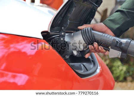 Man's hand with Electric car is charging at the charging station and it is the future of the Automobile.