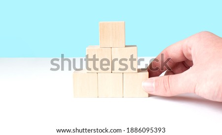 Man's hand establishes a wooden cubes in pyramide. Blank wooden blocks for word, text or illustration. Hand placing cube and finishing the row [[stock_photo]] © 