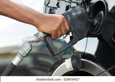 A man's hand filling up a car with gas or petrol at a gas station.