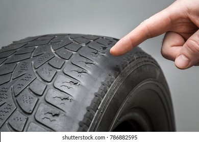 Man's hand finger pointing to the old, damaged and worn black tire tread. Change time. Tire tread problems and solutions concept.