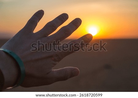 A man's hand in the foreground shielding from the rays of the setting sun in the desert