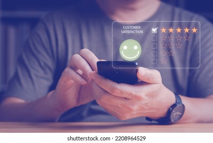 Man's Hand Give The Customer Satisfaction Feedback With Smart Phone, Review And Rating With Five Gold Stars And Smiley Face. Customer Satisfaction Feedback And Survey Concept.