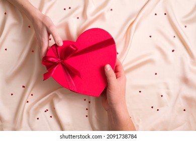 Man's hand gives red heart-shaped gift to female hand. Happy Valentines Day, Happy Birthday concept.