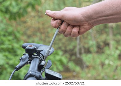 man's hand with gray screwdriver tightening screw on black metal bicycle handlebar on summer street - Powered by Shutterstock