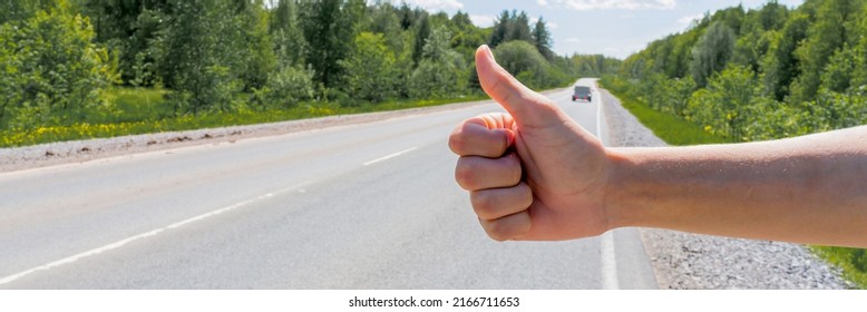 A man's hand and a hitchhiking sign on the road, hitchhiking around the city. The man tries to stop the car with his thumb up. Adventure and tourism. High quality photo