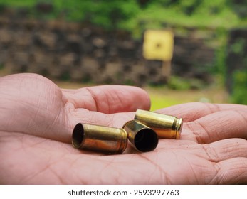 A mans hand hold an empty shells of bullet chasing of 9mm caliber pistol on shooting range field.