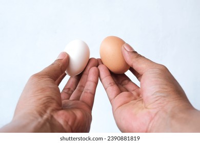 man's hand holding 2 eggs of different colors isolated on white background - Powered by Shutterstock