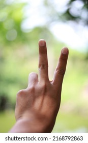 Man's Hand Holding Up 2 Fingers On A Green-yellow Blur Background.