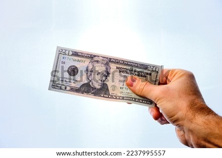 Man's hand holding a 20 dollar note, on a white background.