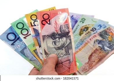 Mans Hand Holding Australian Dollar Banknotes Against New Zealand Dollar Bank Notes. Concept Photo Of Money, Banking ,currency And Foreign Exchange Rates.  (Isolated On White Background)