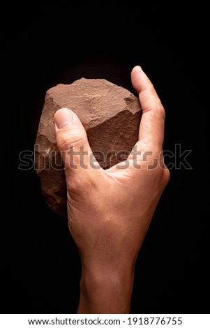 Man's hand holding a beautiful well preserved paleolithic quartzite splitter on a black background