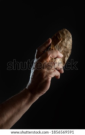 A man's hand holding a bifacial-backed knife. Knife carved in flint from the Middle Paleolithic, on black background