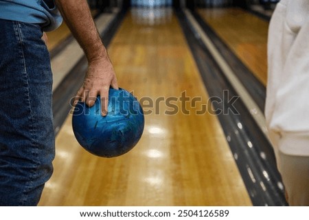 Man's hand holding blue bowling ball at bowling alley in club close-up
