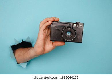 Man's Hand Holding Camera From Blue Torn Paper