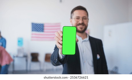 Man's hand holding cell phone with green screen. Blurred male showing green display. People filling out ballots while choosing new candidate for President in polling station. - Powered by Shutterstock