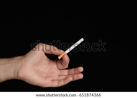 Man's hand holding a cigarette between index finger and thumb in the shape ring. isolated on black background