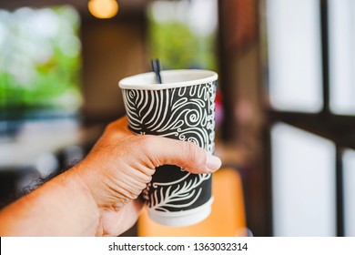 A man's hand holding a cup of hot black coffee by the restaurant window
