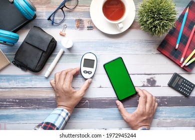 Man's Hand Holding Glucose Meter And Smart Phone On Table 