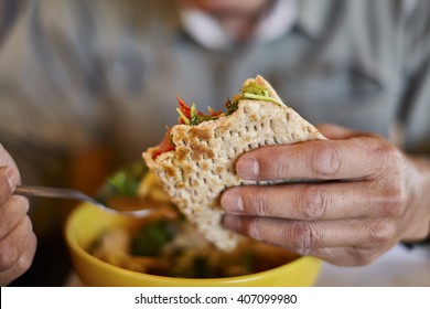 Man's Hand Holding A Half Eaten Flatbread Sandwich Over A Bowl Of Soup