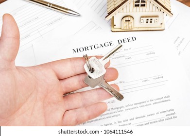 Man's Hand Holding Keys Of House Over Mortgage Deed.