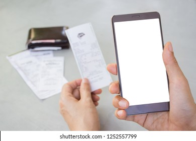 Man's Hand Holding Mobile Phone With White Screen And Holding Bill Or Slip With Blurred Leather Wallet And Utility Bills On Grey Table Background