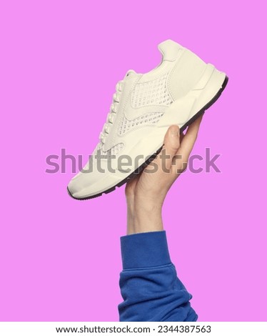 Man's hand holding a modern white sneaker isolated on a lilac background. Sport and active lifestyle. Footwear sales advertising campaign