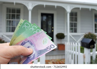 Man's Hand Holding New Zealand Dollar Currency Bills Against A Traditional Villa House In Auckland, New Zealand. Buy, Sale, Real Estate, Insurance, Mortgage, Bank Loans And Housing Market Concept. 