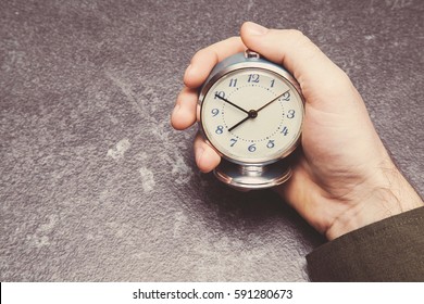 Man's hand holding an old table clock. Time tracking. Vintage retro style.
