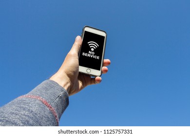 Man's Hand Holding A Phone, And Tries To Find A Signal Vayf Against The Blue Sky. On The Phone Screen, The Symbol With No Signal.