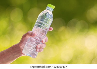 Man's Hand Holding Plastic Water Bottle On Blurred Green Bokeh Background