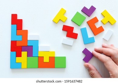 man's hand holding a square tangram puzzle, over wooden table - Shutterstock ID 1591637482