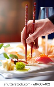A man's hand holding sushi with red chopsticks luxury serving