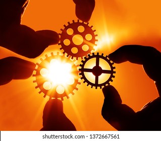 Man's Hand Holding Three 3 Wooden Cog Gear Wheel On Blue Sky Background. Sunshine And Yellow Sky . Sun Rays. Business Team Concept. 