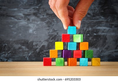 man's hand holding a top of wooden blocks pyramid over wooden table ,human resources and management concept.
