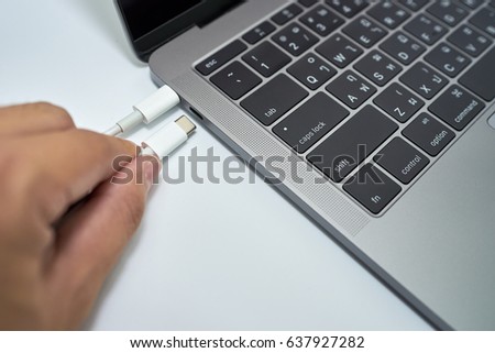 Man's hand holding USB type C cables to connect or disconnect to laptop computer on white background