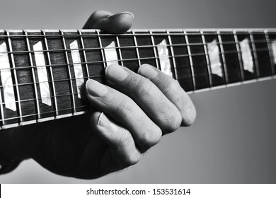 Man's hand holding vintage guitar fretboard and playing notes with fingers on strings.