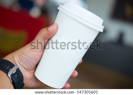 man's hand holding white empty paper coffee cup with a plastic cap